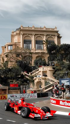 a man driving a red race car down a street in front of a large building