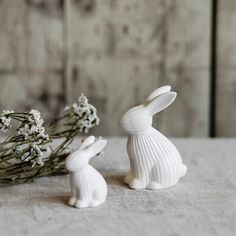 two white ceramic rabbits sitting next to each other on top of a table with flowers in front of them