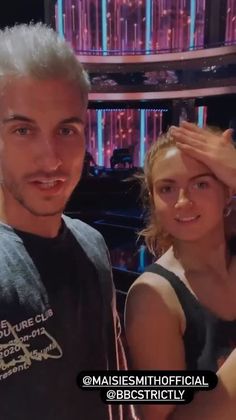 a man and woman standing next to each other in front of a tv screen with neon lights