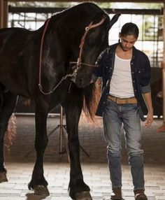 a man is walking with his horse in the stable