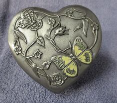 a heart shaped box with flowers and butterflies on it's sides, sitting on a blue surface