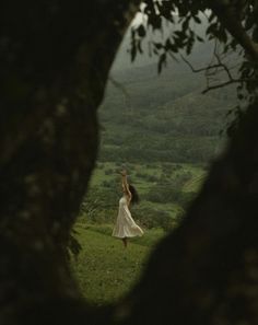 a woman in a white dress standing on top of a lush green field under a cloudy sky