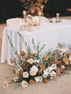 an arrangement of flowers and candles on a table with a white linen draped over it