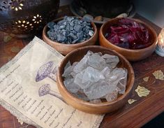 three wooden bowls filled with different types of rocks on top of a table next to a lit candle