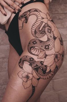 a woman's thigh with a snake and flowers tattoo on the side of her leg