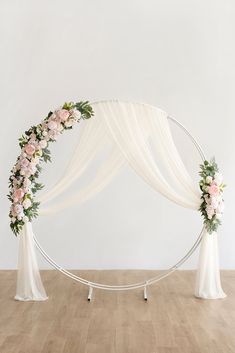 an arch decorated with white flowers and greenery for a wedding ceremony in the middle of a wooden floor