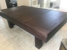 a large wooden table sitting in the middle of a room with tile flooring and white walls