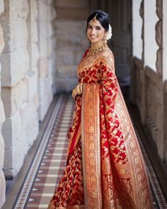 a woman in a red and gold bridal gown standing on a tiled floor next to an archway