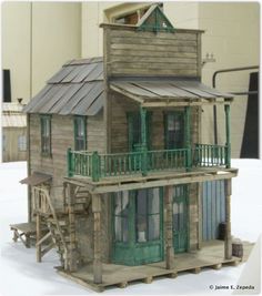 a doll house made out of wood with green trimmings and a porch on the second floor