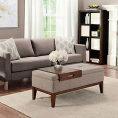 a living room with a couch, ottoman and coffee table in front of a window