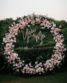 a wedding arch decorated with pink flowers and the words you me written in cursive writing