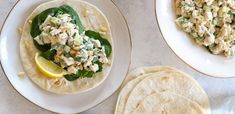 two plates with tortillas and salad on them next to some lemon wedges