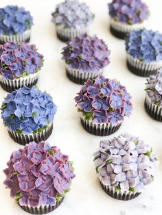 cupcakes decorated with purple and blue flowers on a white table top, ready to be eaten