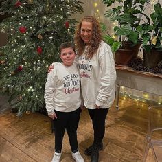 two people standing in front of a christmas tree