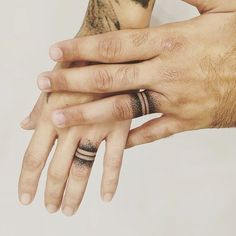 two hands holding each other with tattoos on their fingers and wristbands, while one holds the other's hand