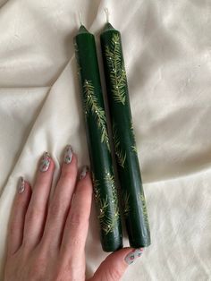 two green candles sitting next to each other on top of a white bed sheet with pine branches