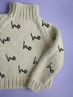 a knitted sweater with words written on the front and back, sitting against a purple background