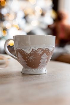 a white and brown cup sitting on top of a table next to a christmas tree