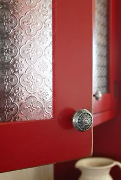 a close up of a red cabinet door with a vase in the corner behind it