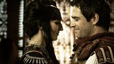 a man and woman dressed in medieval clothing looking at each other while standing next to each other