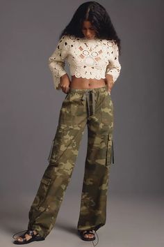 a woman is wearing camouflage pants and a cropped top with crochet detailing