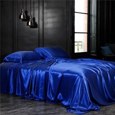 a bed with blue sheets and pillows in a dark room next to an open window