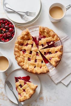 a pie with slices cut out on plates next to cups and saucers, including cherries