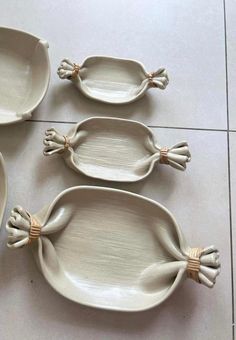 three white dishes with handles and hands on the sides, sitting on a tile floor