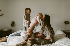 a man laying on top of a bed holding a baby while two other people watch