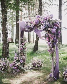 an outdoor wedding setup with purple flowers and greenery on the ground, surrounded by trees