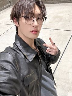 a young man wearing glasses making the peace sign with his hand while standing on concrete