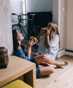 two women sitting on the floor eating pizza