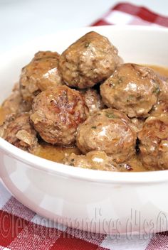 a white bowl filled with meatballs covered in gravy on top of a red and white checkered table cloth