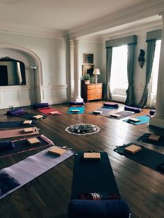 a room filled with lots of yoga mats on top of a wooden floor next to windows