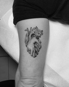 a black and white photo of two hands holding a rose tattoo on the arm,