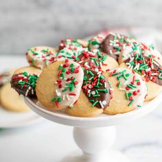 a white cake plate topped with cookies covered in sprinkles and frosting