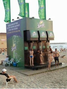 some people are standing in front of a soda machine on the side of the beach