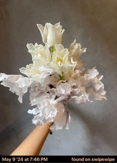 a bouquet of white flowers is held by someone's hand on a gray background