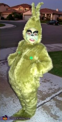 a person in a green bunny costume standing on the sidewalk with their hands behind his back