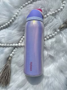 a purple water bottle laying on top of a white fur covered floor next to a tassel