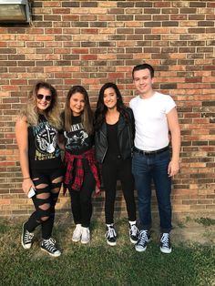 three young people standing next to each other in front of a brick wall and grass