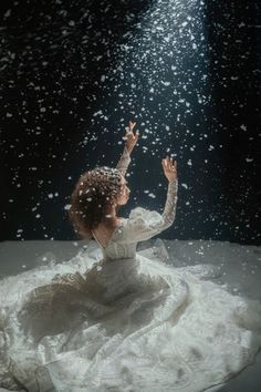 a woman sitting on top of a bed under a light shining through the air above her head