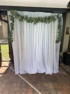 a white curtain with green leaves hanging from it's side on a brick floor