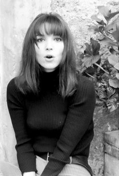 a black and white photo of a woman sitting on the ground with her hands in her pockets