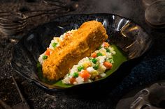 two pieces of fried fish and rice in a black bowl with utensils on the side