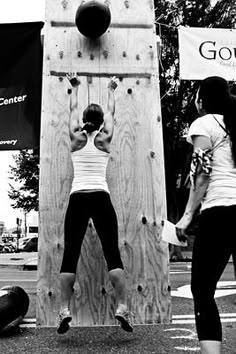 two women doing pull ups in front of a wooden structure with banners on the side