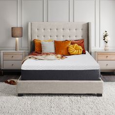 a white bed with orange and yellow pillows on it in a large room next to two nightstands