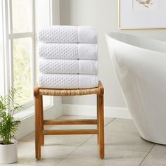 a stack of white towels sitting on top of a wooden chair next to a bath tub