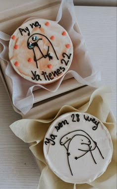 two decorated cookies in a box with writing on them