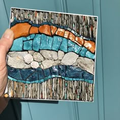 a hand holding up a piece of art made out of rocks and pebbles on a blue door